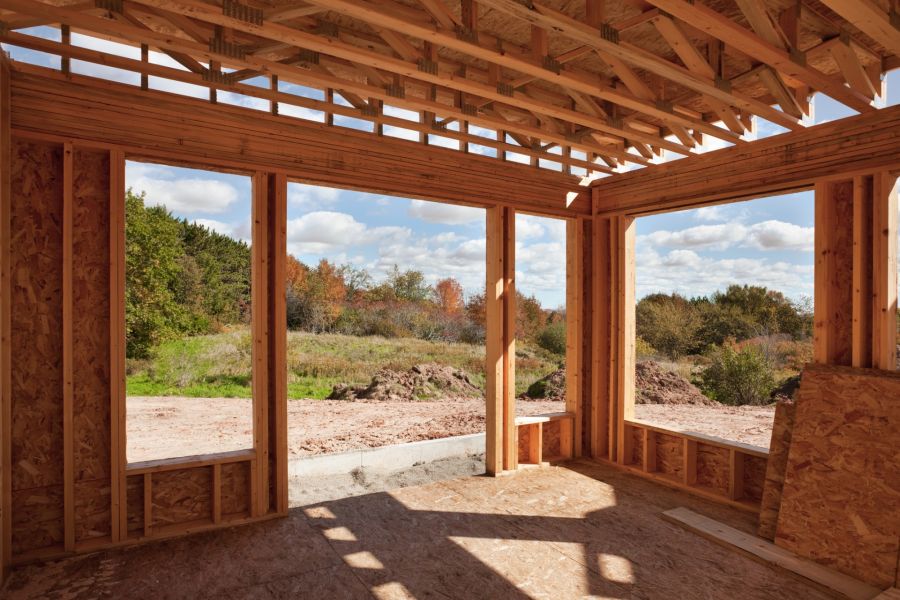 Unfinished home addition framing with large window openings and exposed roof trusses overlooking a backyard