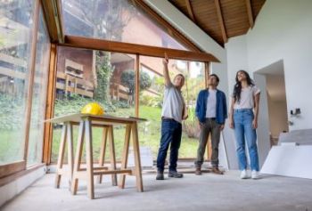 Three people inspecting a modern house under construction with large windows and exposed wooden beams